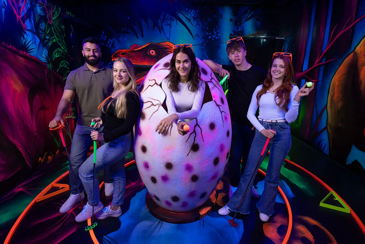Gruppe posiert mit Dino-Ei im Schwarzlicht Minigolfbereich