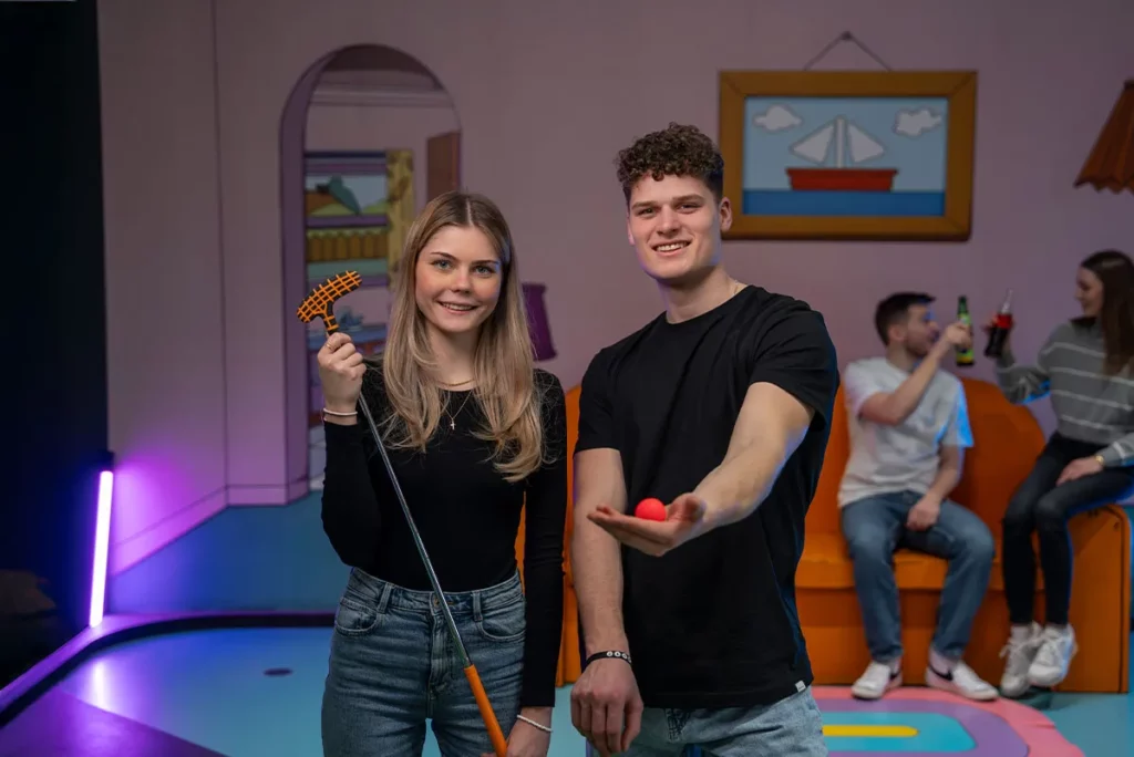 Zwei Personen mit Ball und Schlaeger in Minigolfhalle