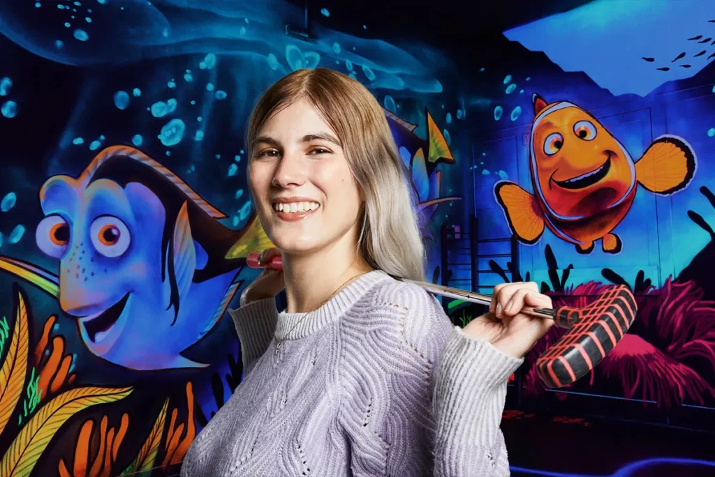 Junge Frau mit Schlaeger vor Unterwasserwand mit Clownfisch